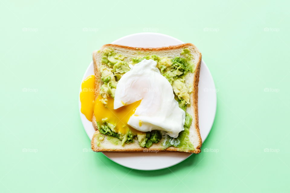 Sandwich with fresh green avocado, poached egg on white plate