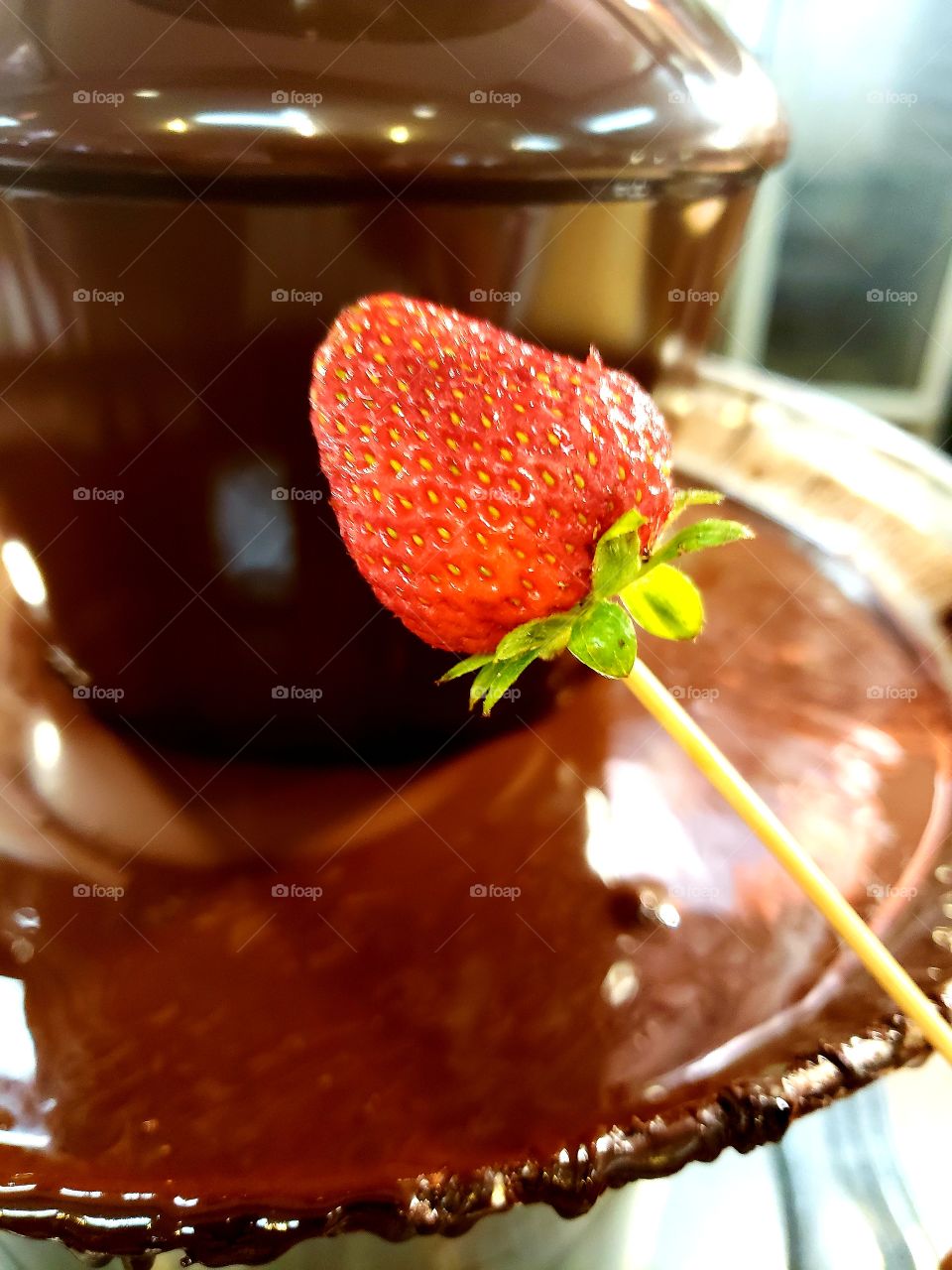 Ripe strawberry about to be dipped in chocolate fondue. The perfect combination.