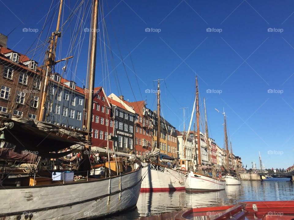 Canal filled with large sail boats, colorful buildings line the canal. They are tall with many windows. 
