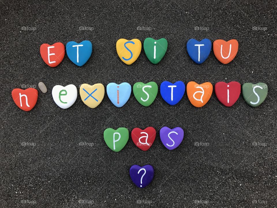 Et si tu n'existais pas ? French love declaration with colored heart stones over black volcanic sand