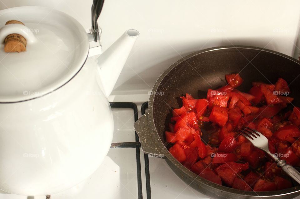 White enameled kettle on a white enameled gas stove next to a pan full of chopped tomatoes