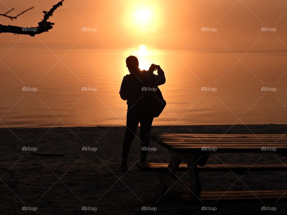 A young lady prepares to photograph a majestic , colorful and descending sunset over the bay. 