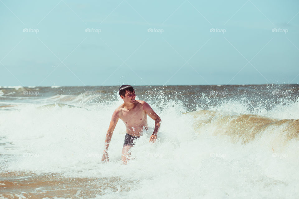 Young man enjoying the high waves in the sea during a summer vacations. Spending a summer holiday by the sea