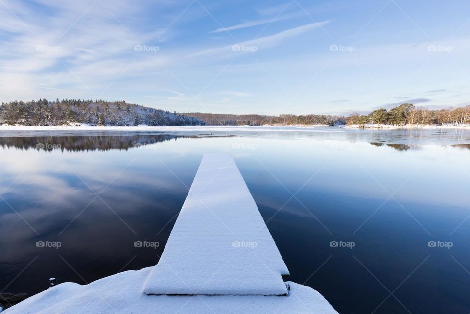 Peaceful beautiful winter day by the lake with reflection , snow covered pier in partly frozen water 