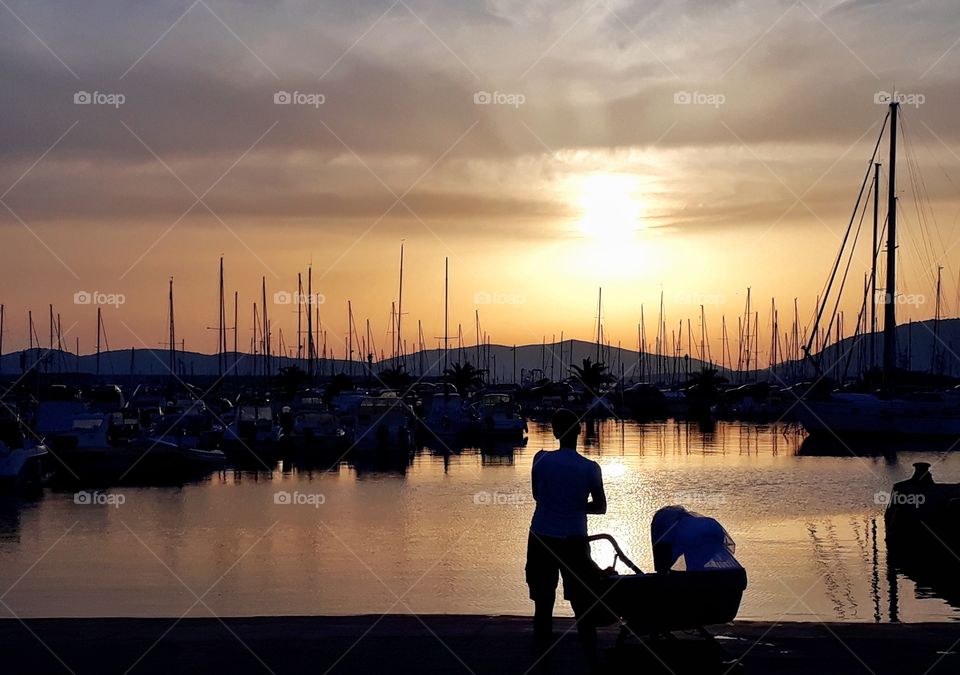 Mom lulling a baby in front of sea sunset view . Alghero, Italy
