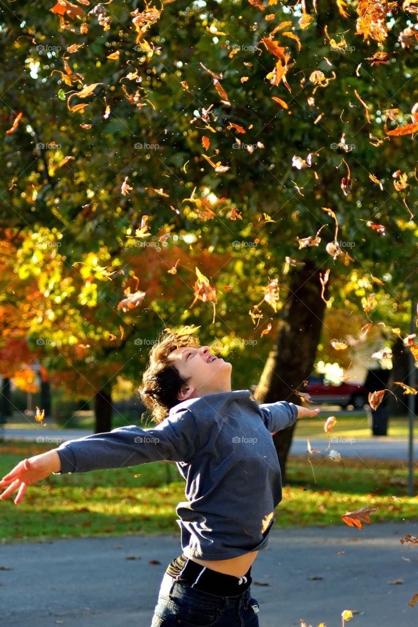 Close-up of a happy boy with falling autumn leaves