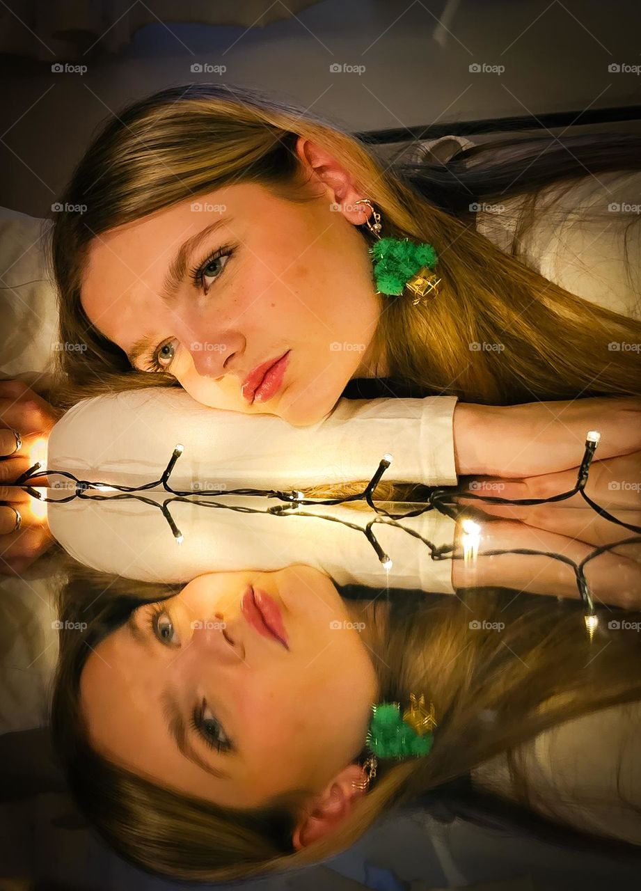 The beautiful girl, lying at the mirror. She is a beautiful girl, with Christmas look. Christmas ear Decoration and Christmas light. Beautiful girl.