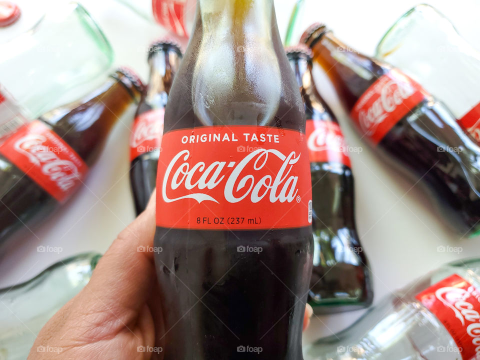 Holding a Coca-Cola bottle with Coca-Cola bottles in the background.