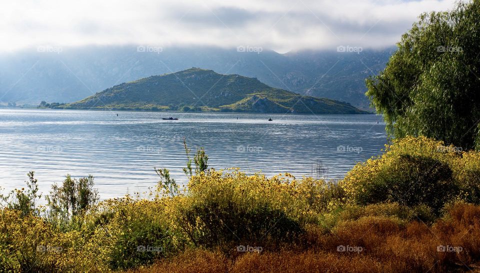 Boaters on a lake with an Islam in the middle on an overcast day.