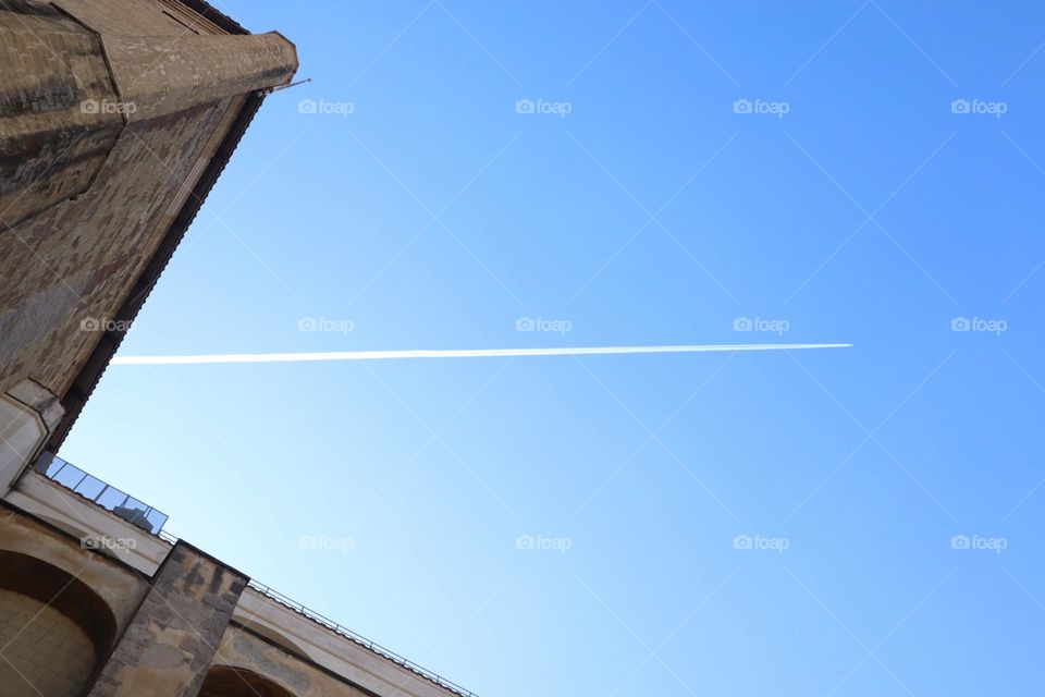 White jet plane line on blue sky between buildings tops