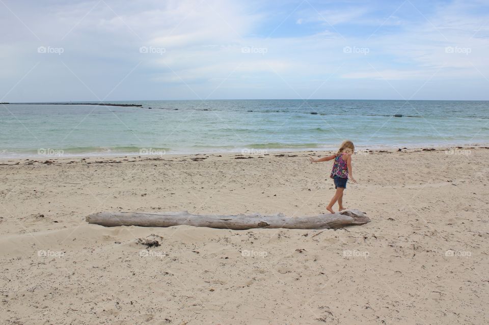 Little girl balancing on driftwood at the ocean