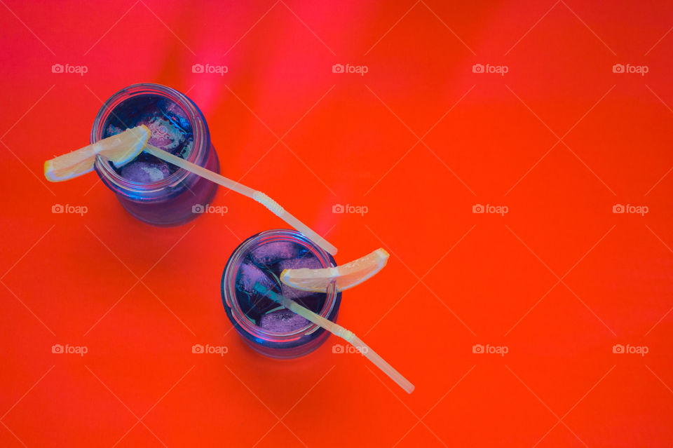Two blue cocktails with lemon slices and straws on a red background top view.