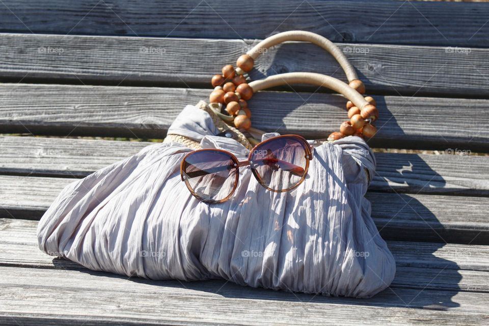 Summer handbag and sunglasses on a bench in the sun