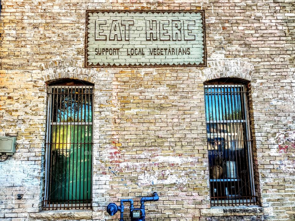 Painted sign on brick wall between two windows: Support local vegetarians