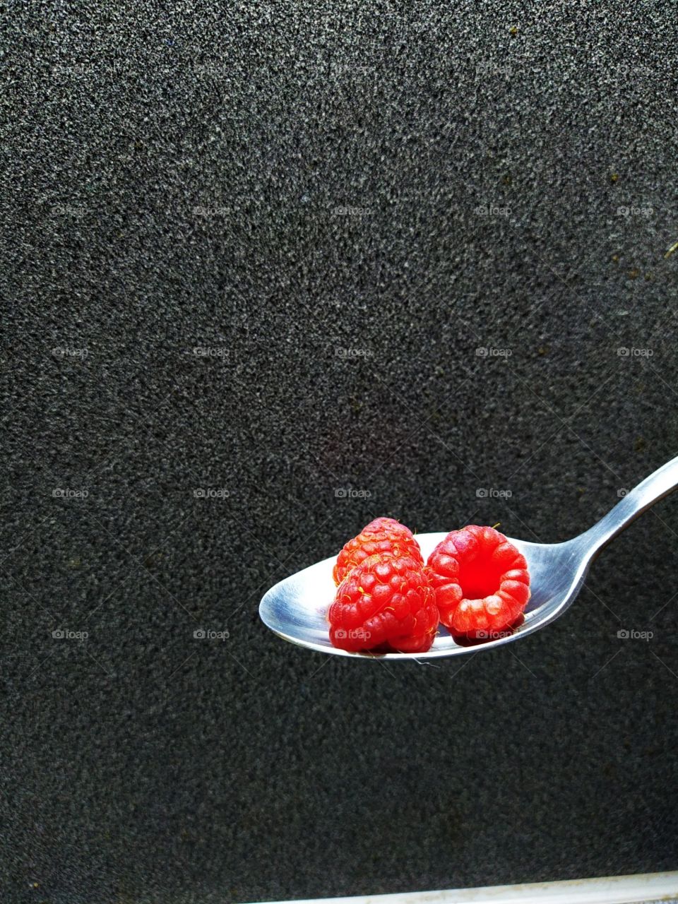Three red raspberry berries in a silver metal spoon