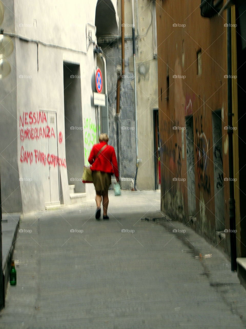 old woman walking in a narrow street wearing a red jacket