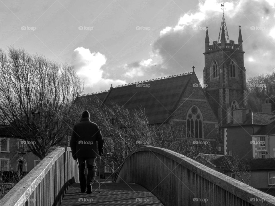 Man on walking over wooden bridge with church in the background