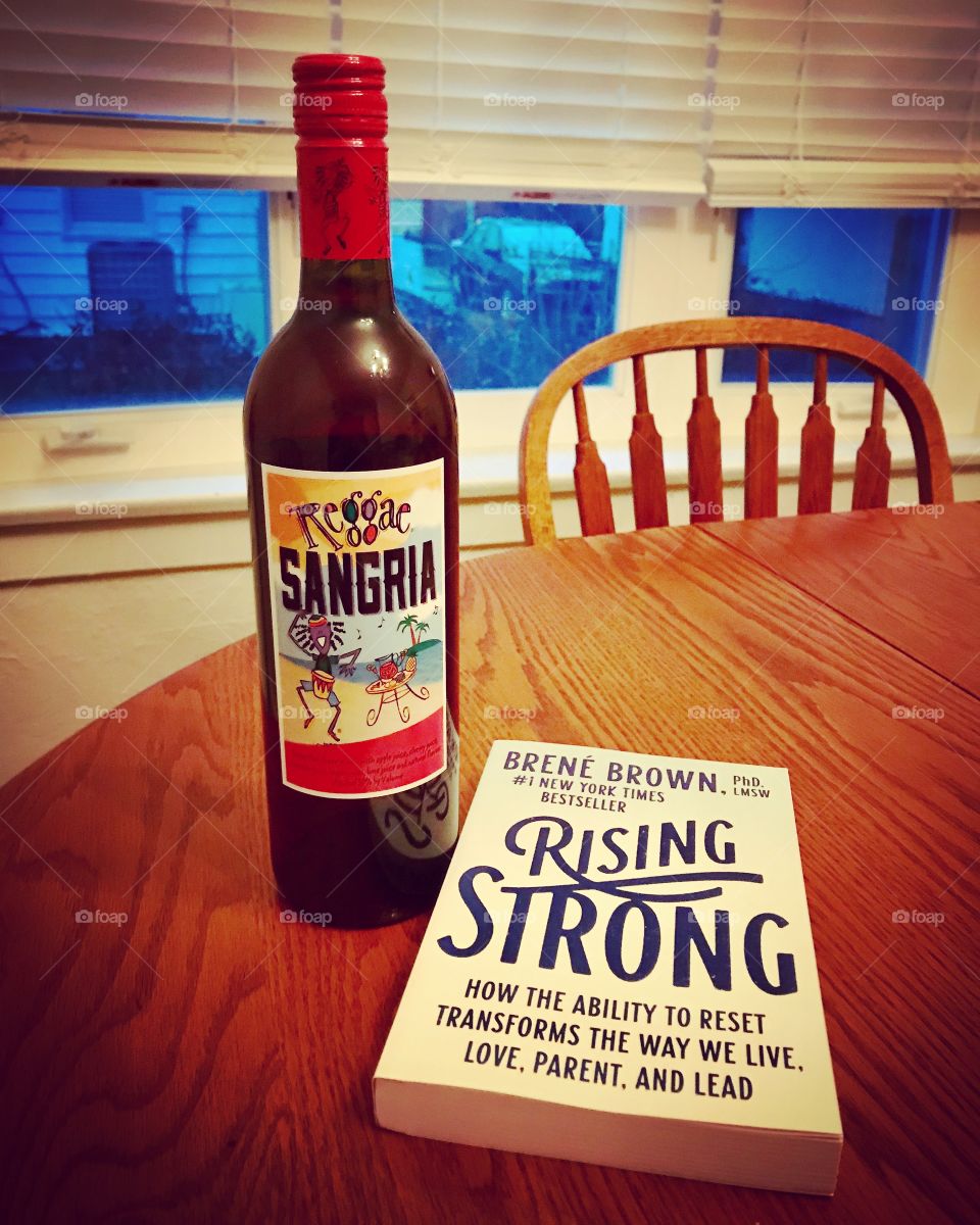Reggae red wine bottle and Brene Brown book on wooden table 