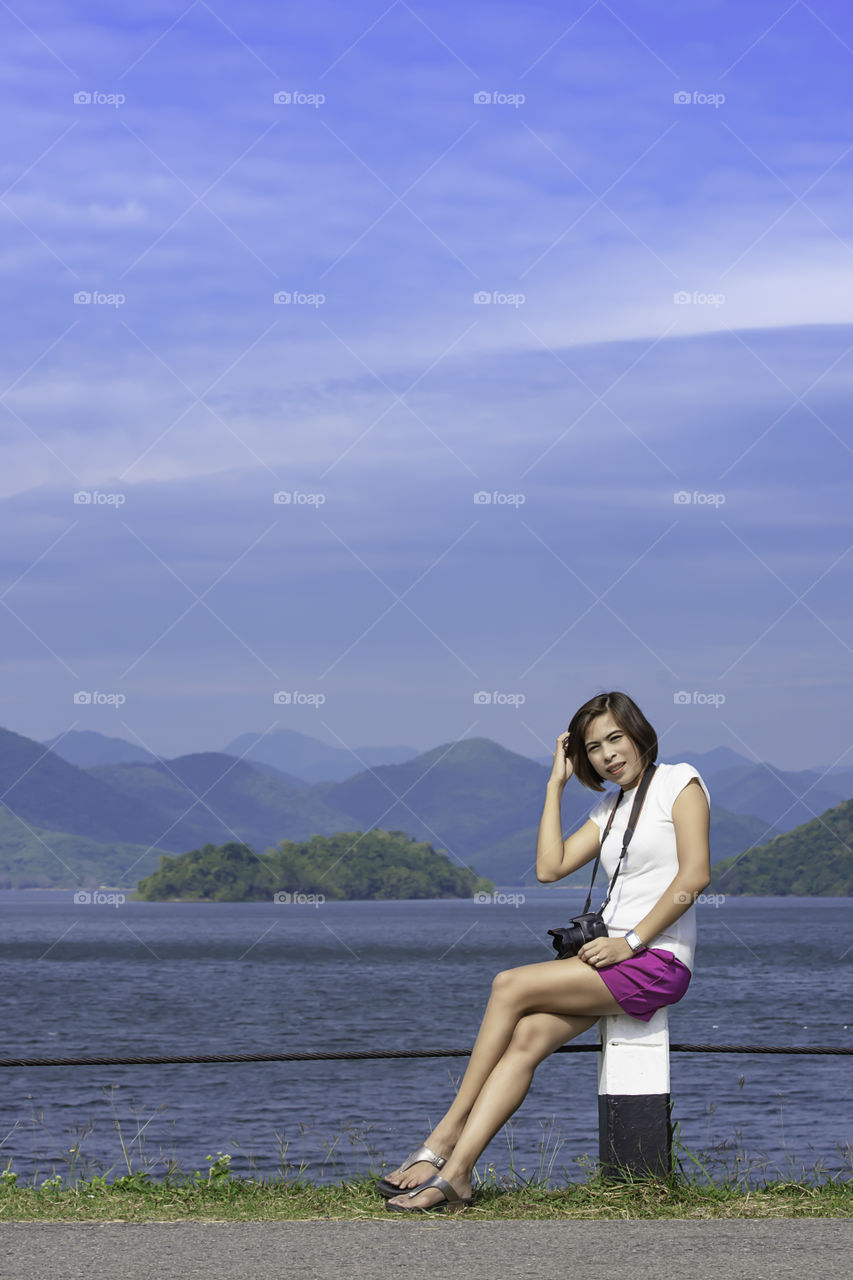 Women and the camera sitting on a concrete pillar at Kaeng Krachan dam phetchaburi , Thailand.