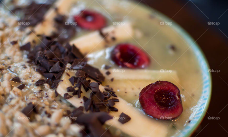Colorful sweet fruit smoothie bowl garnished with antioxidant rich dark cacao chocolate shavings, banana and cherry with oatmeal healthy breakfast artisanal food photography 