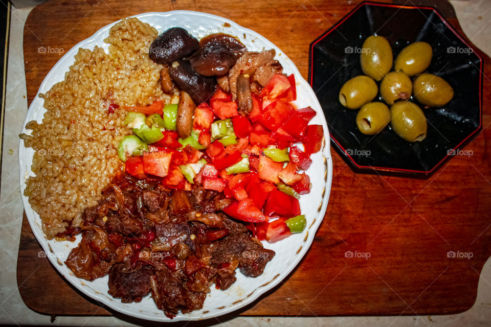 Served on a plate: chopped beef prepared in soy sauce, tomato chopped with chopped green peppers, rice with soy sauce; second tanner: large green olives