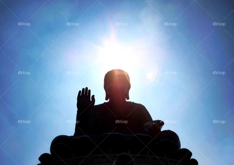 Selective focus silhouette Tian tan buddha and light flare on blue sky background