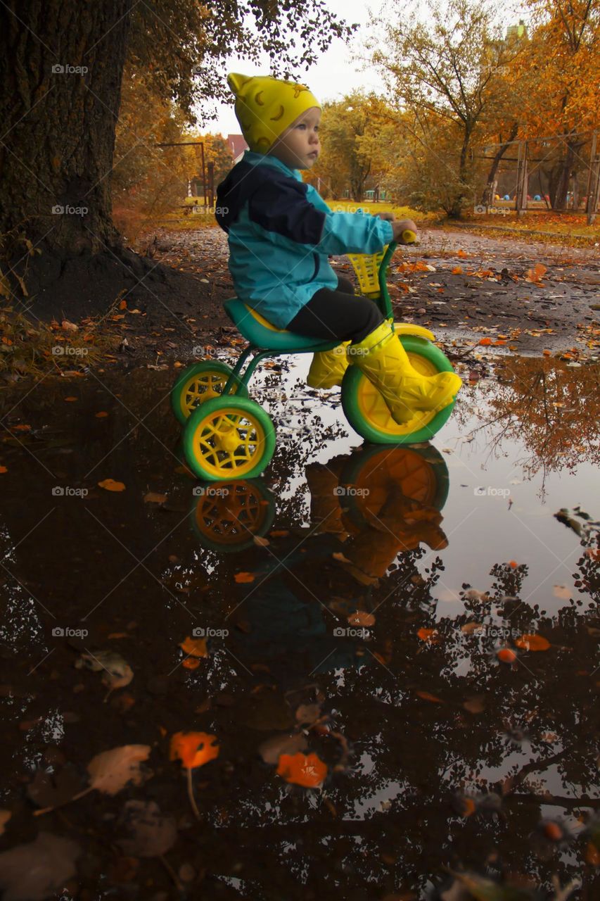 A little boy in yellow boots is learning to ride a bike in the park.