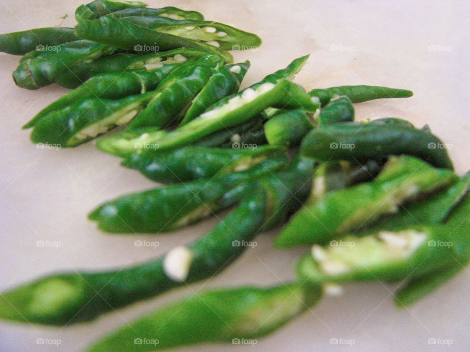 Close-up view of a number of green chilies that have been cut and placed on a white cutting board surface in high angle view