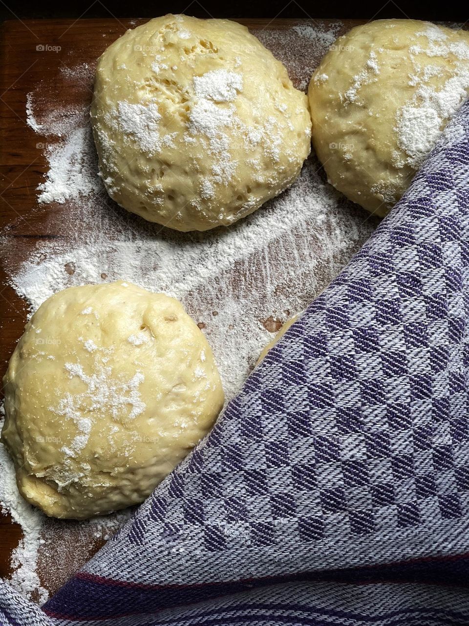 Fresh yeast dough formed into balls lies on a wooden board dusted with flour