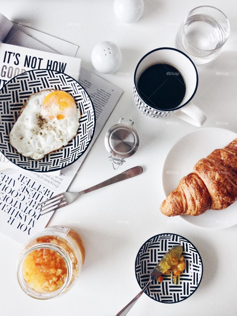 Simply breakfast with wholewheat croissant, orange fruit spread, fried egg and black coffee.