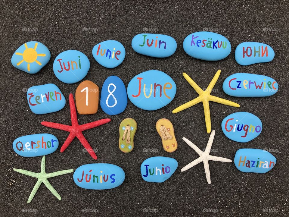 18 June, calendar date with multicolored stones and starfishes over black volcanic sand