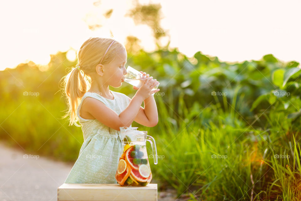 Cute little girl with blonde hair drinking homemade lemonade outdoor 
