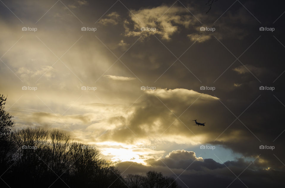 An airplane flying towards the storm clouds at sunset 