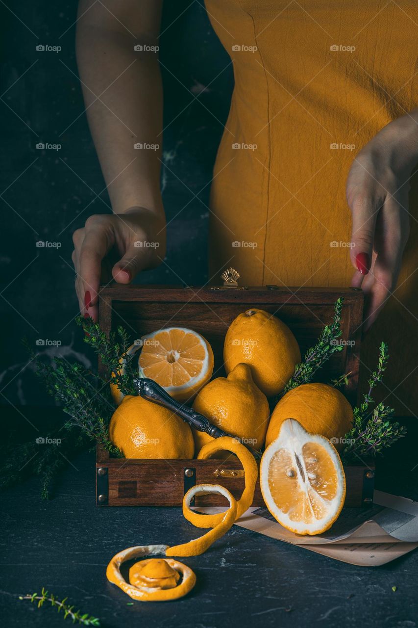 a girl in a yellow dress stands behind a casket full of juicy lemons. Conceptual photography. Fruit Still life