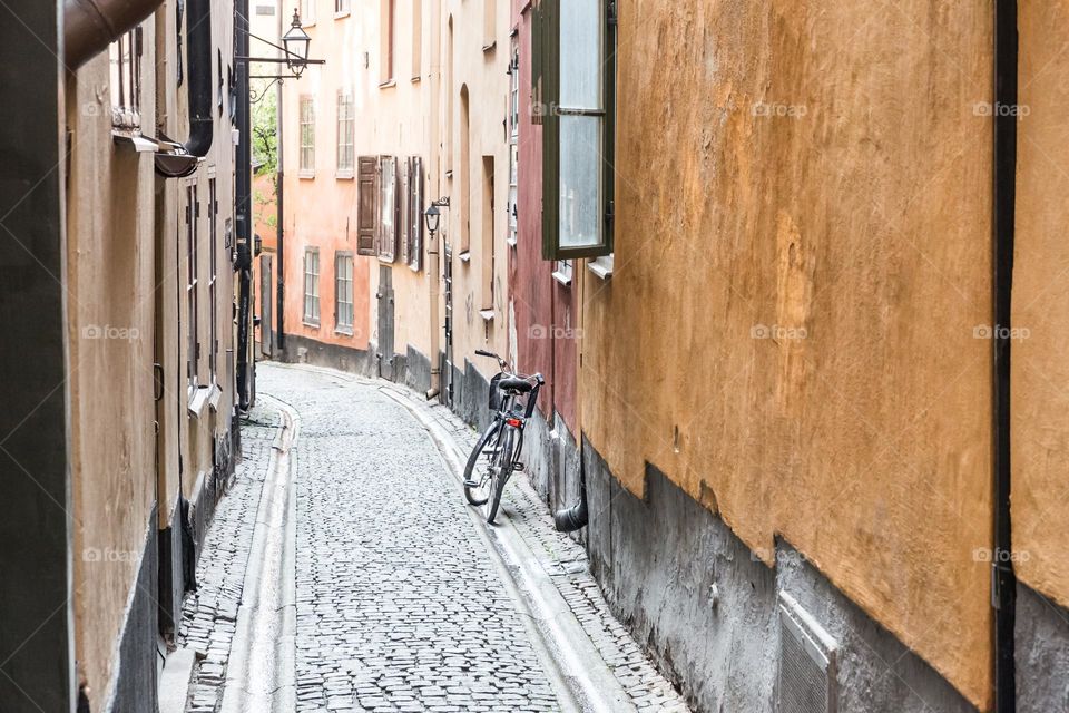 One lonely bicycle parked in an empty old narrow alley with colorful buildings , no people 