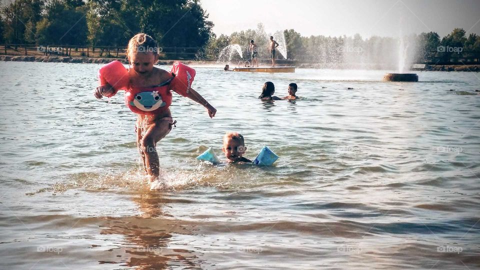 Children playing in lake with fountains in background