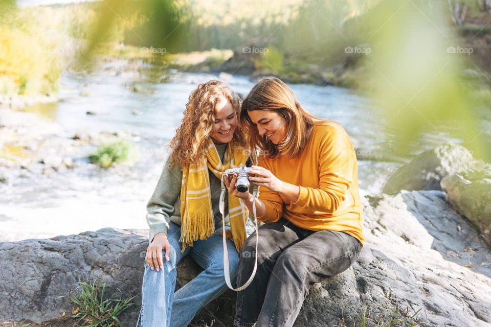 Young women travellers friends taking photos on camera on view background of mountains and river, hiking on the autumn nature