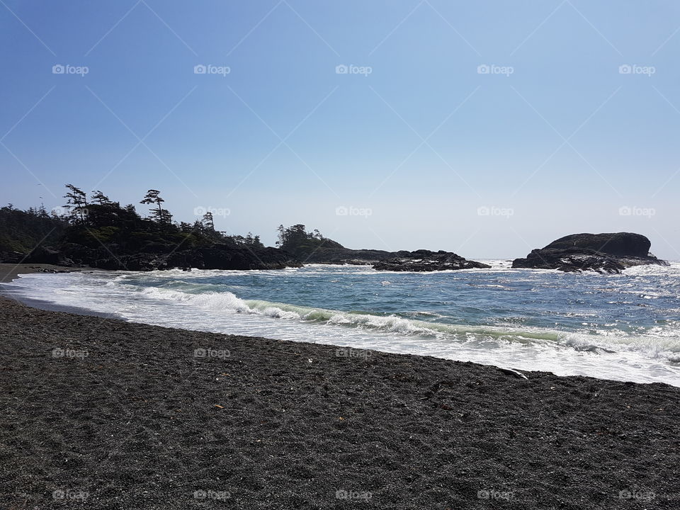 bright sunny clear sky summer day outside, sandy beach with white cap waves of the blue ocean in Tofino, Canada