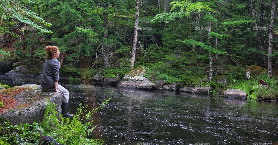 A woman sits on a rock overlooking the river, enjoying the beauty of the forest and moving waters.