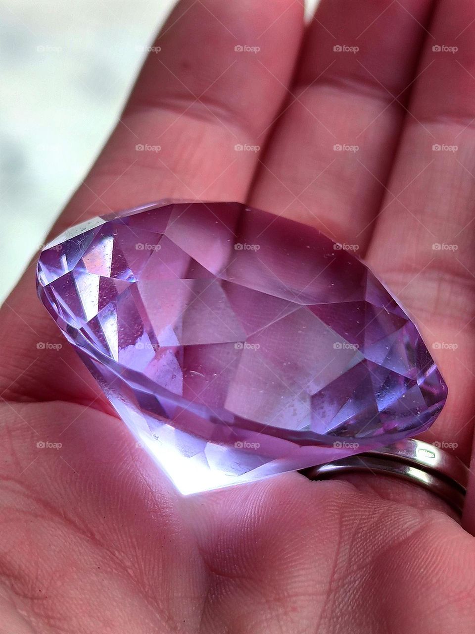 In the hand lies a large cut purple rock crystal. The edges of the crystal are flawless. Purple crystal is clean like a tear and even fingers under it are visible
