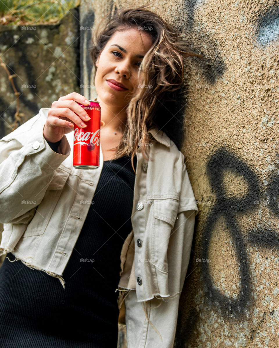 Leaning against a wall with a coca cola beverage.