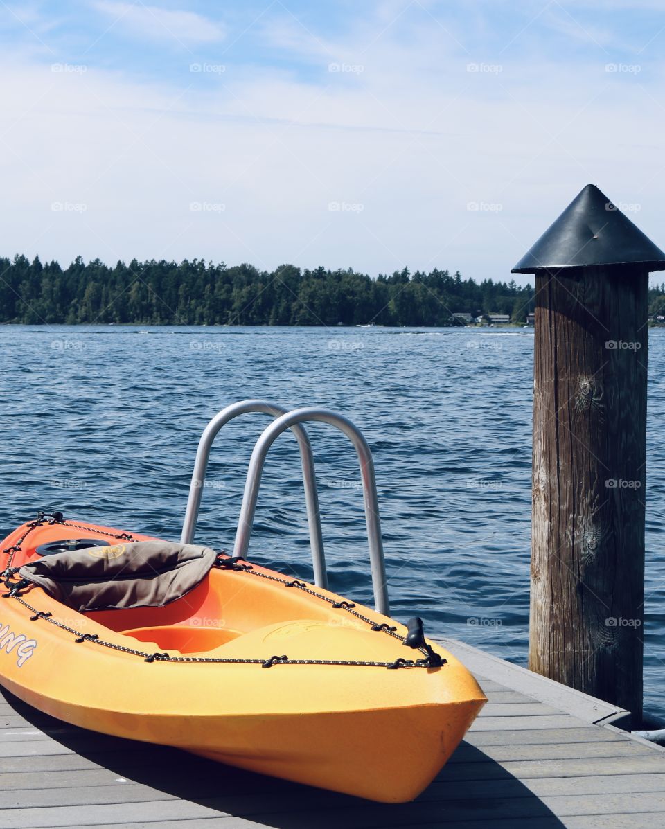 A bright orange kayak is placed on a lakeside dock in Washington State in preparation for use