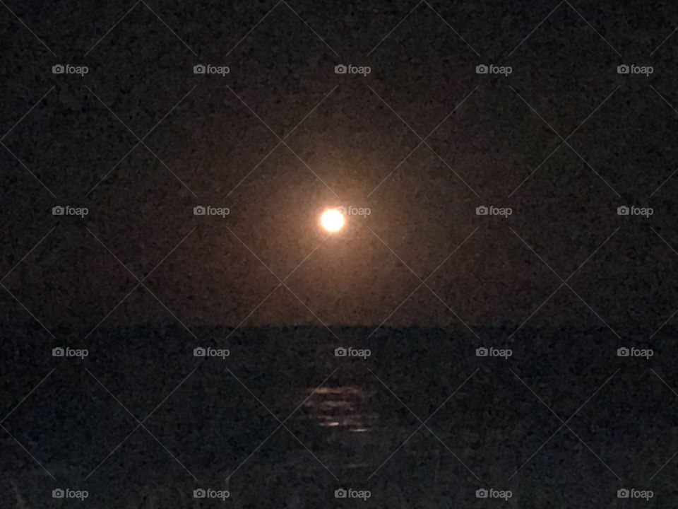 A full orange moon in a black sky reflecting on the ocean