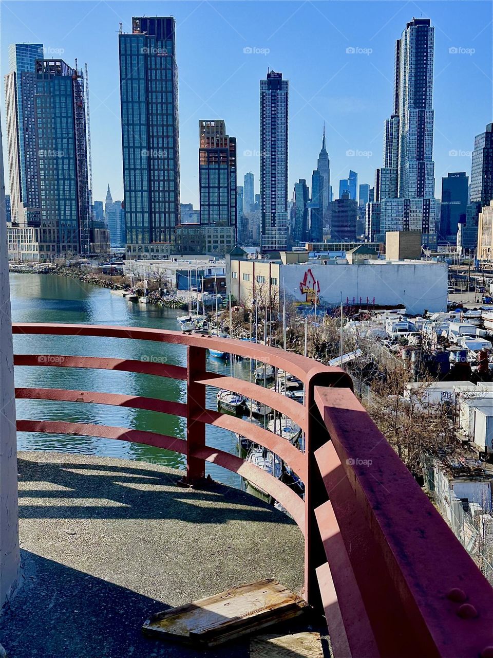 This is “Newtown Creek” seen from the central outpost of the “Pulaski Bridge” that connects “Greenpoint”, Bklyn to LIC. Straight ahead you see LIC and in the furthest distance “Manhattan” incl. the “Empire State Bldg”. 2024. Hypnotic Productions