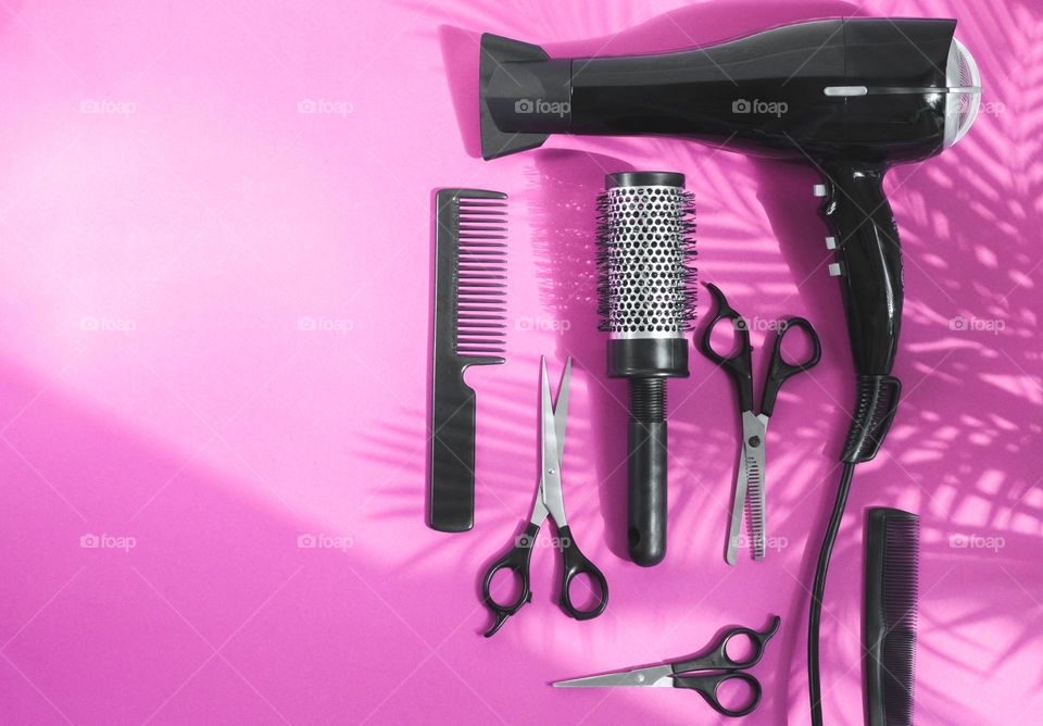 Set of hairdressing tools from: hair dryer,combs and scissors lie on the right on a lilac background with a shadow of a palm branch and a copy of the space on the left,flats Lay, close-up. The concept of the barbershop.