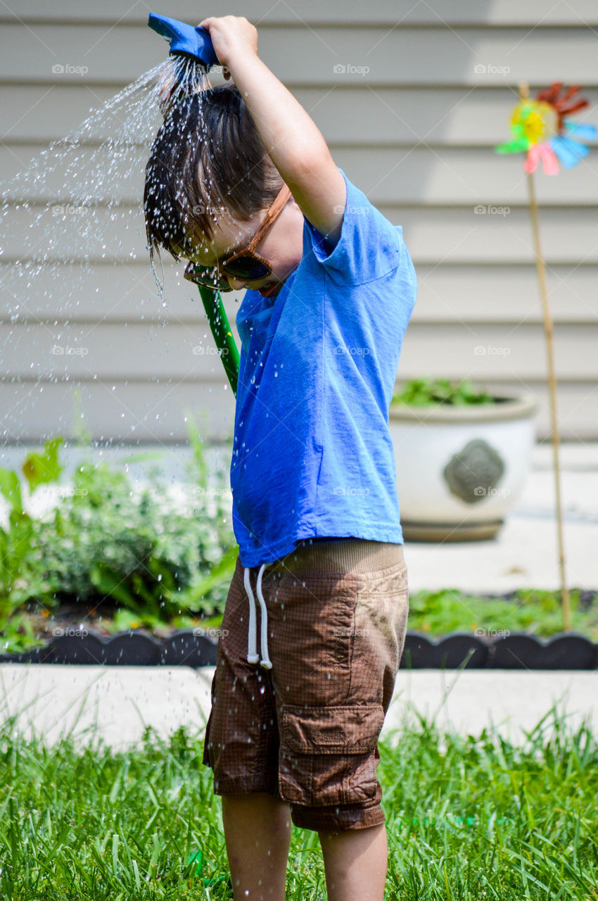 Young boy using a garden hose to spray himself in the summertime