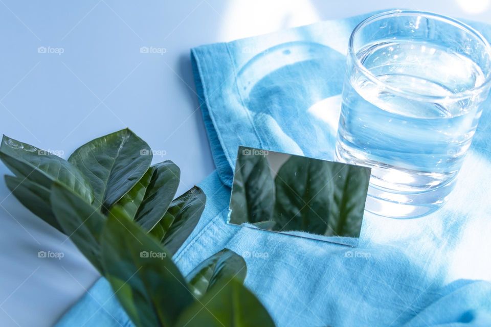 Items and image are selected and prepared for travel. A blue shirt, a glass of clean water and sunglasses, reading magazines on a blue background.