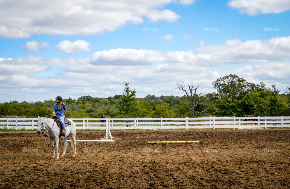 Young woman on a white horse in the middle of a field with blue skies