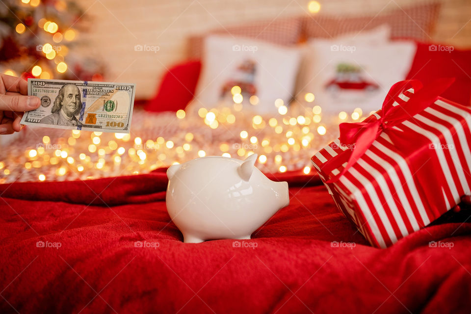 piggy bank with 100 dollars banknote in festive New Year atmosphere of scenery.  Magical bokeh with Christmas tree and bright lights.