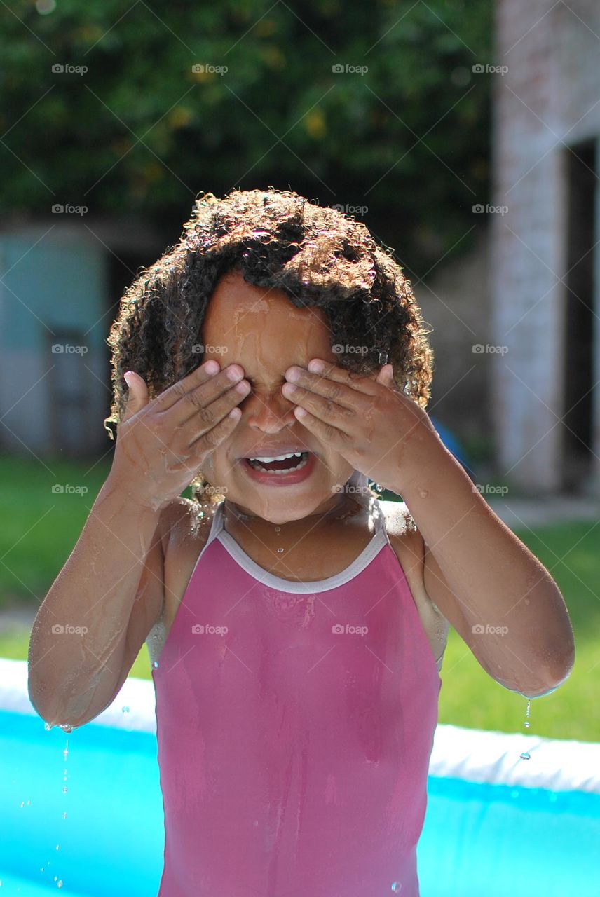 Cute little girl enjoying some playtime in a swimming pool during a hot summer day, looking for refreshment